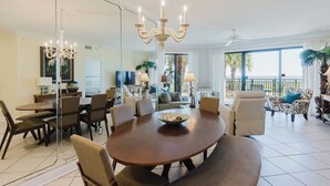 Ein geräumiges Wohnzimmer mit einem großen runden Tisch, bequemen Sitzgelegenheiten, einer Chandelüster und einem Balkon mit Blick.