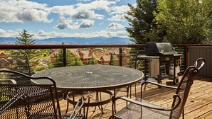 A deck with a round metal table and chairs, a grill, and a view of houses and mountains. - JHRL - Snow Ridge #5 - Slopeside Mountain Lodge Decor, close walk to the base (Teton Village)