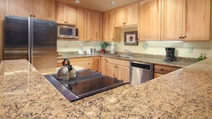 A kitchen with wooden cabinets, stainless steel appliances, granite countertops, a kettle, and a coffee maker. - JHRL - Snow Ridge #5 - Slopeside Mountain Lodge Decor, close walk to the base (Teton Village)