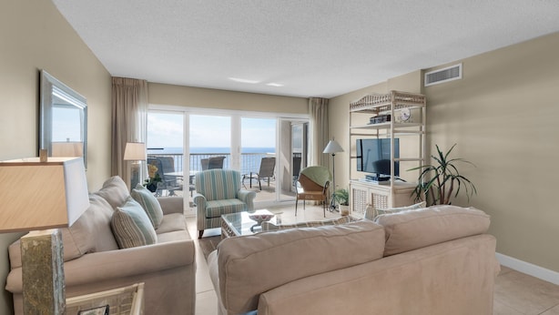 A spacious living room with a large sofa, a coffee table, and a television. There is a balcony with a view of the ocean. - Sand Key 714:  2 BR / 2 BA Gulf Front Condo in Perdido Key, FL  Sleeps 6 (Pensacola)