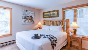 Cama bem arrumada com chapéu e manta xadrez, cabeceira de madeira, duas luminárias de cabeceira e obras de arte nas paredes.