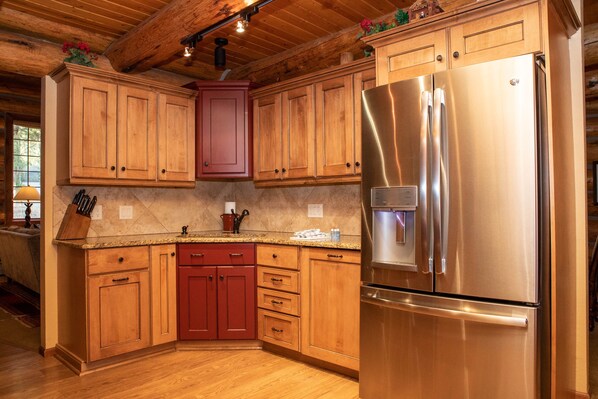 A kitchen with wooden cabinets, a stainless steel refrigerator, and a marble countertop.