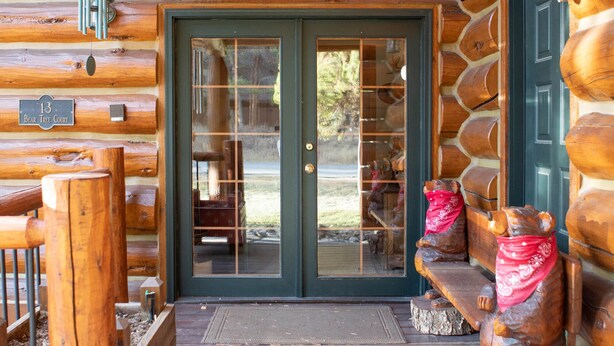 A log cabin with a wooden porch, a glass door, and a stone bench with bear statues. - Luxury Custom Log Cabin Retreat in Keystone/Large Private Patio (Keystone)