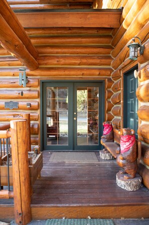 A log cabin with a wooden porch, a glass door, and a stone bench with bear statues.