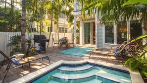 Un patio trasero con piscina, barbacoa y mobiliario exterior.