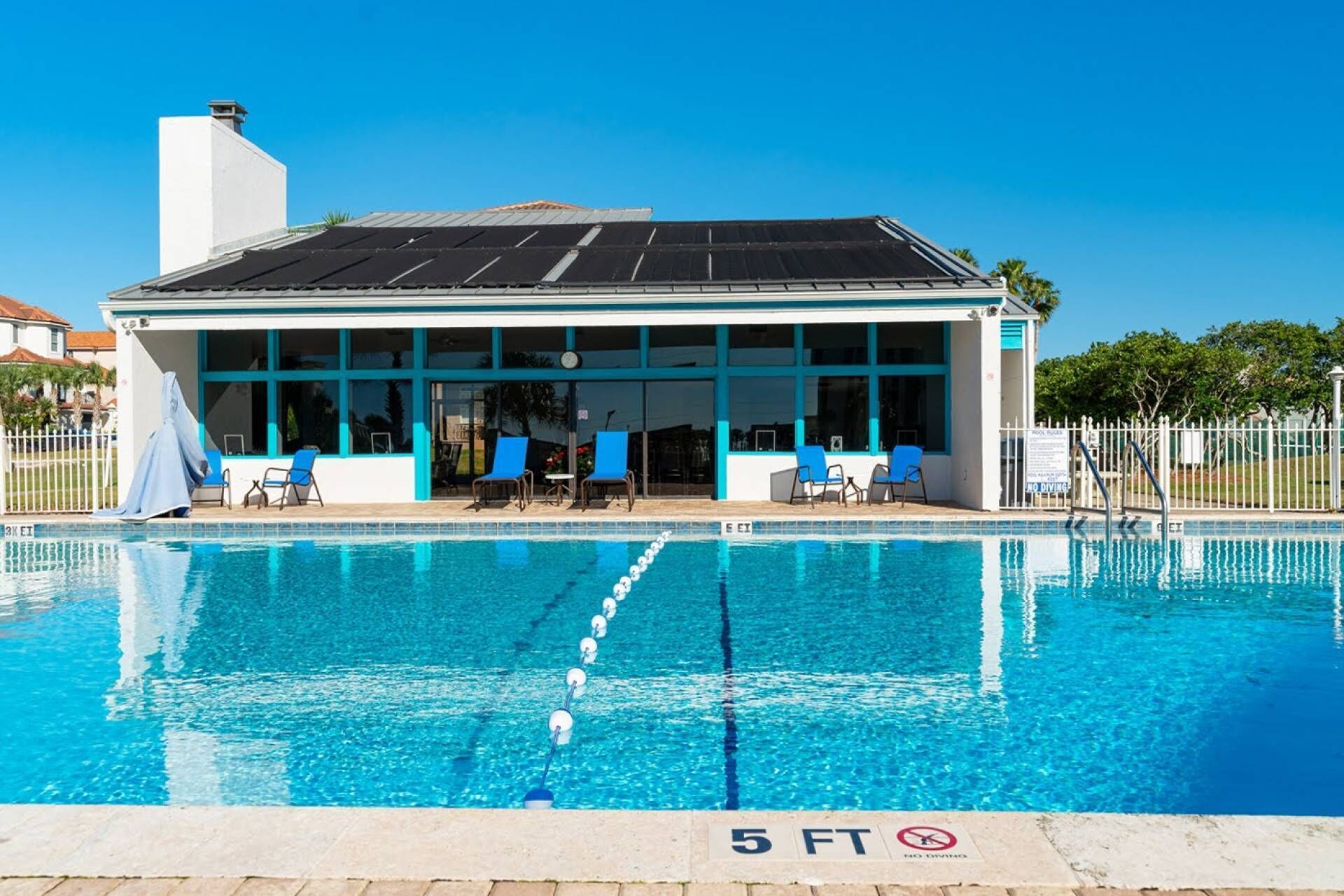 A swimming pool with a covered area, lounge chairs, and a clear sky.