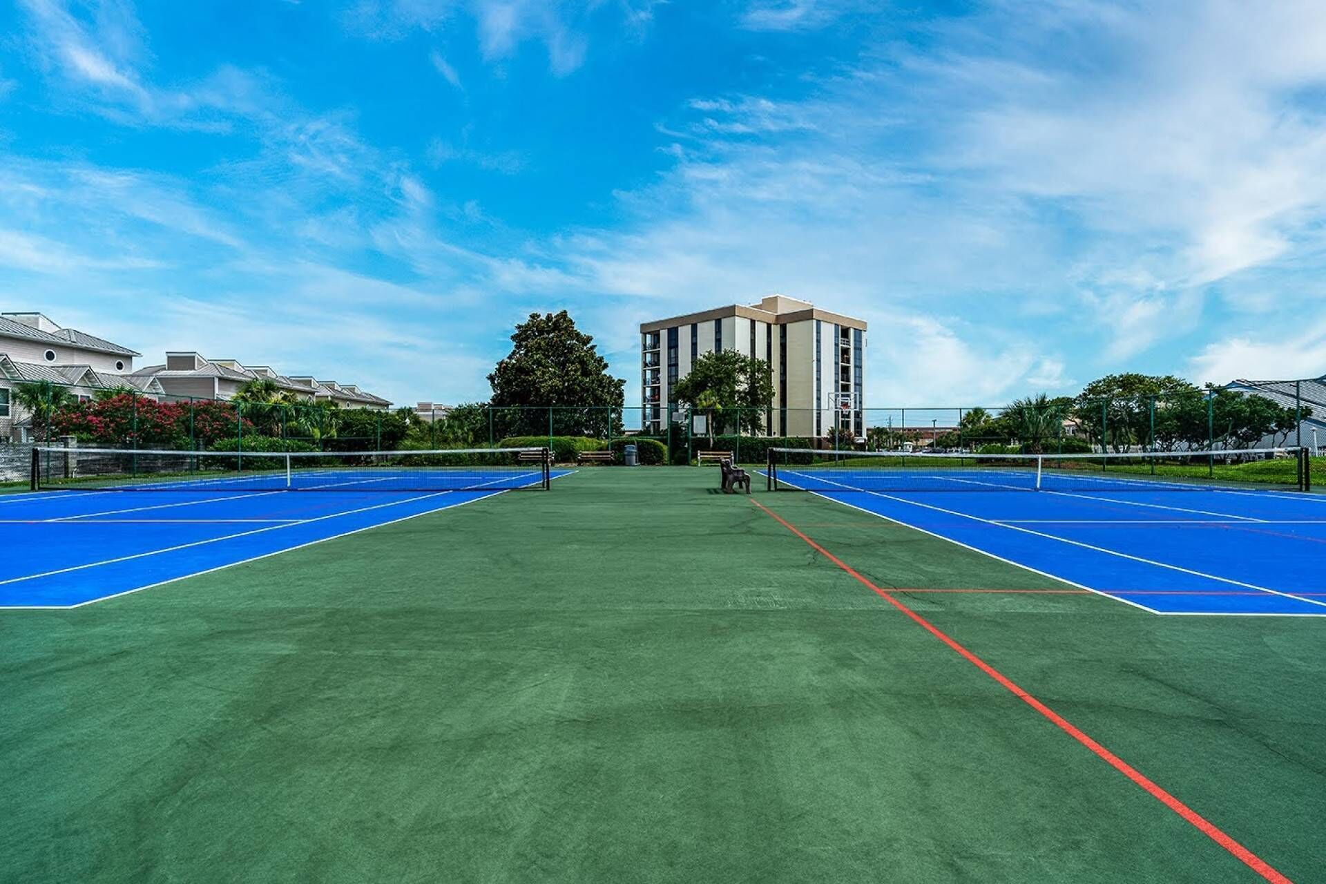Una cancha de tenis con dos superficies azules, un campo verde y un edificio al fondo.