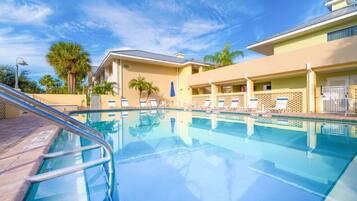 A clear swimming pool with lounge chairs and palm trees in the background.