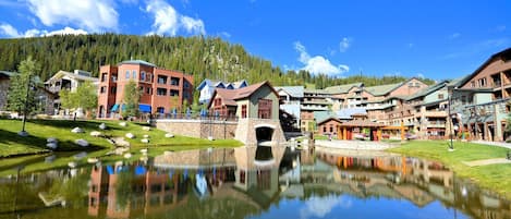 Un resort a orillas del lago con un puente central, edificios que se reflejan y montañas al fondo.