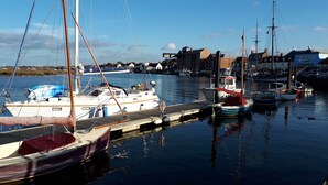 A marina with several sailboats docked, a wooden pier, and buildings in the background. - Well Cottage in Central Holt Norfolk.  Cosy. Sleeps 4 adults. Free Parking. (Holt, Norfolk)