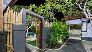 Une entrée fermée par un portail, agrémentée d’une clôture en bois, d’un mur en béton et d’un petit jardin avec des plantes et un sentier.