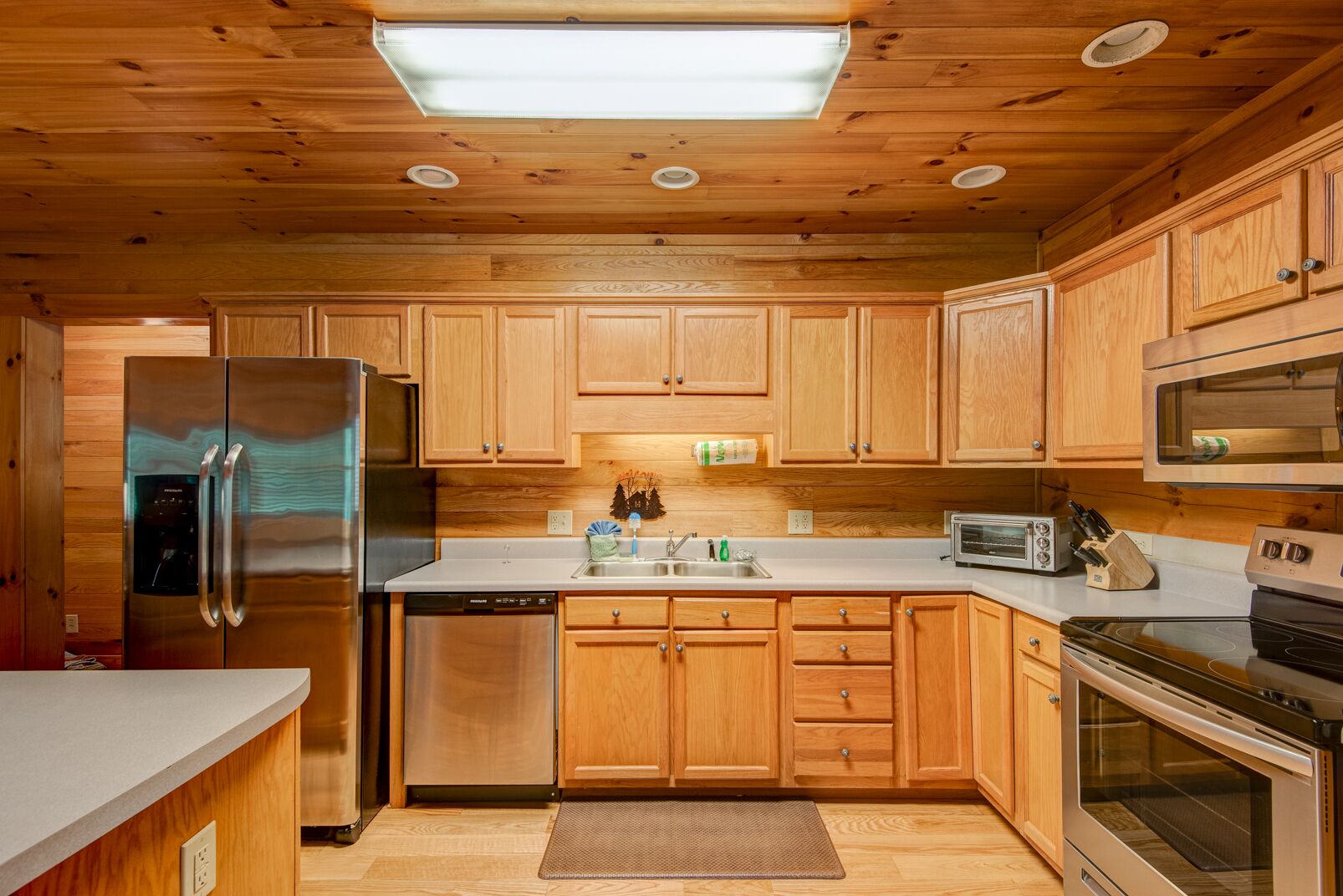 Una cocina con armarios de madera, un refrigerador de acero inoxidable, un lavavajillas, un fregadero, un tostador y un horno.