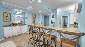 Una cocina con armarios blancos, una isla de madera con taburetes de bar y un espejo grande.