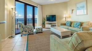A living room with a television, sofa, and chairs, a ceiling fan, and a view of the ocean through large sliding doors. - Spectacular Gulf Front Views in this 3BR Condo! (Orange Beach)