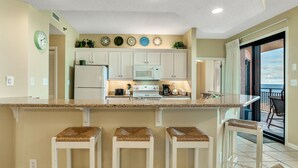A kitchen with white cabinets, a granite countertop, and three bar stools. - Spectacular Gulf Front Views in this 3BR Condo! (Orange Beach)