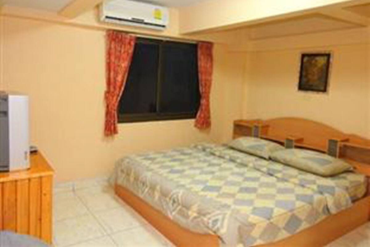 A bedroom with a bed, a wooden dresser, a window with curtains, and a painting on the wall.