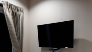 Ein Hotelzimmer mit einem Bett, einem an der Wand montierten Fernseher und einem Vorhang.