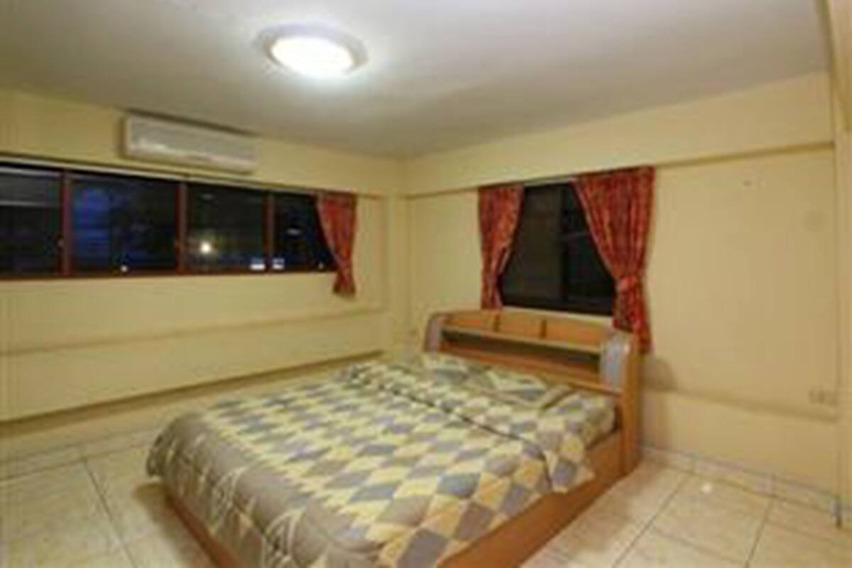 A bedroom with a bed, a window with curtains, an air conditioning unit, and a tiled floor.