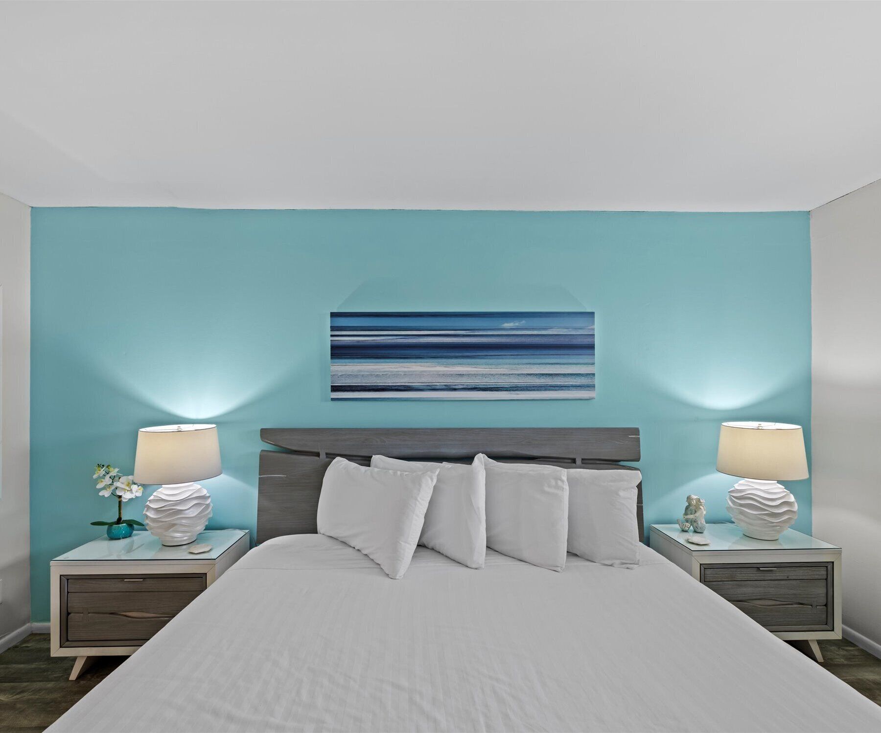 Ein Schlafzimmer mit einem Bett, zwei Nachttischen, einem Wandbild und einer dekorativen Vase.