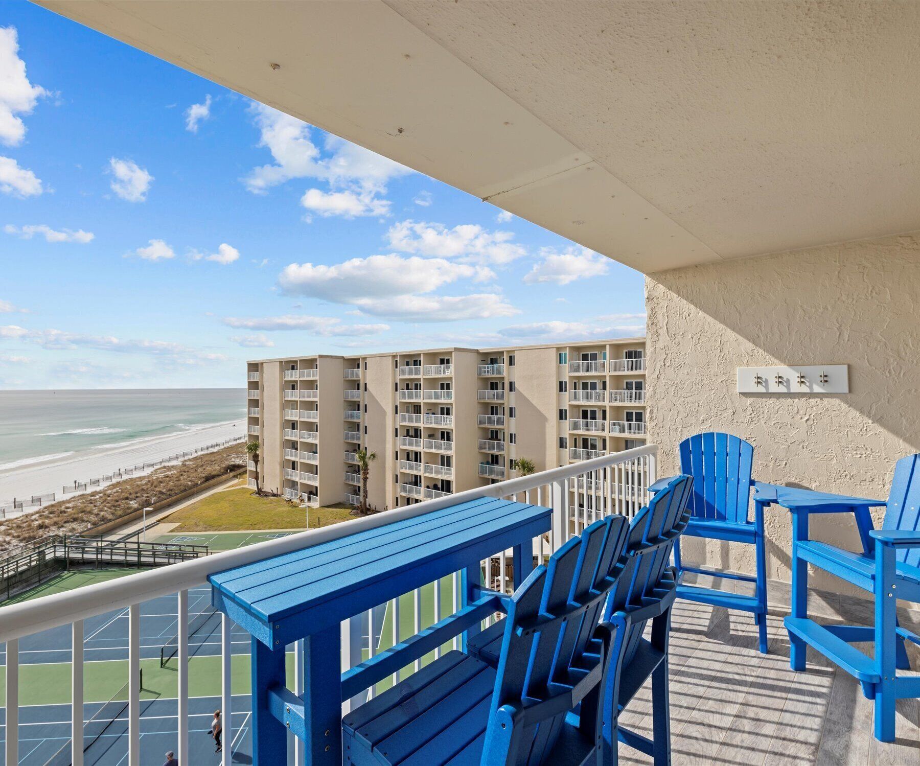 A balcony with blue chairs overlooking a beach and a multi-story building.