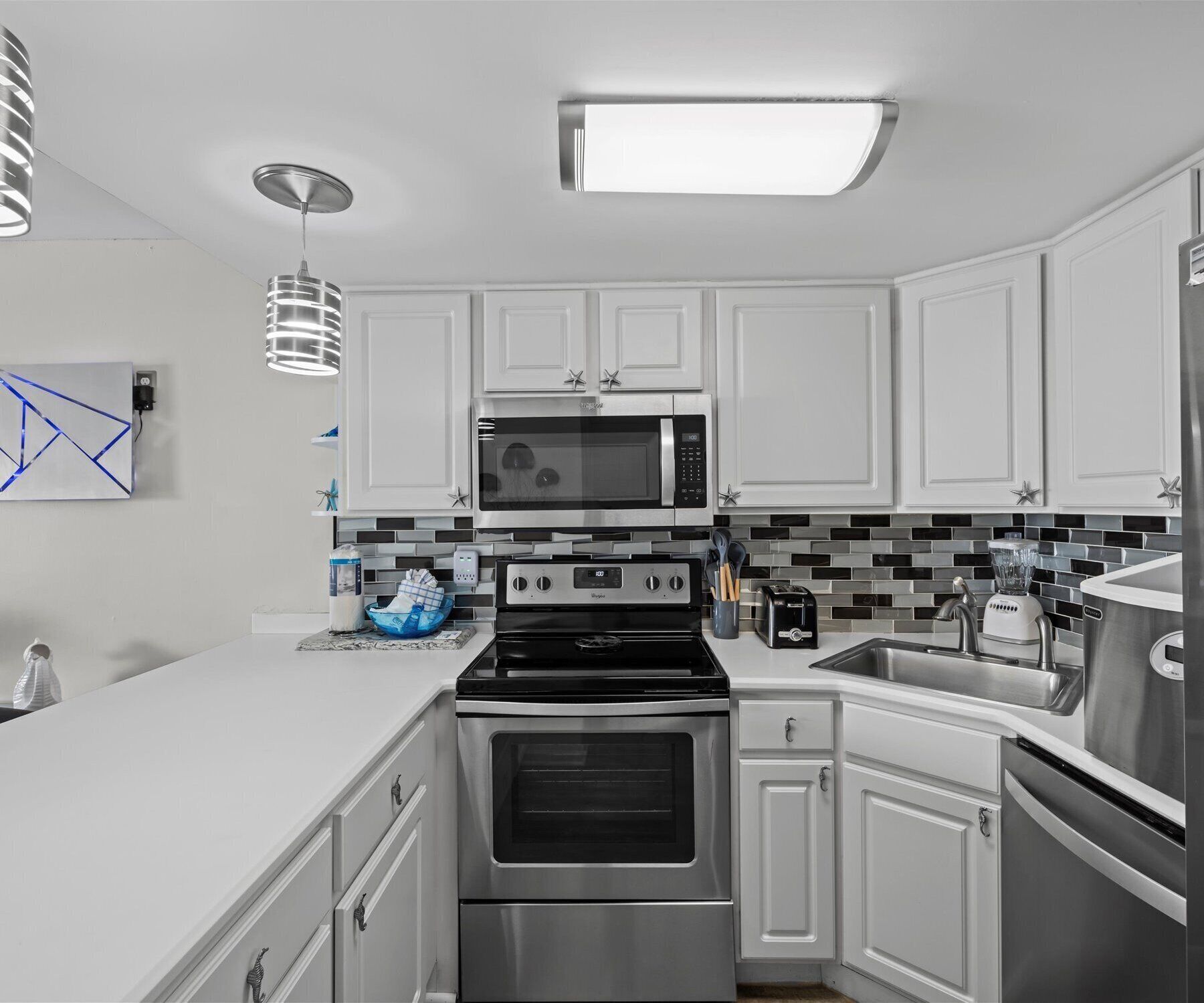 A modern kitchen with white cabinets, a black and silver stove, a microwave, and a stainless steel refrigerator.