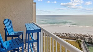 Un balcón con vista a la playa, que incluye dos sillas Adirondack azules y una barandilla blanca.