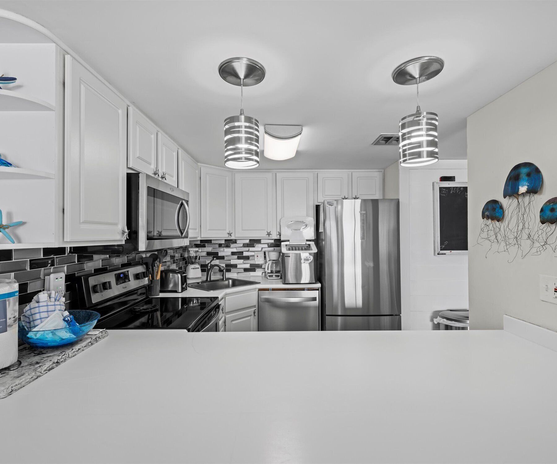 Une cuisine moderne avec des armoires blanches, des appareils en acier inoxydable et des luminaires suspendus.