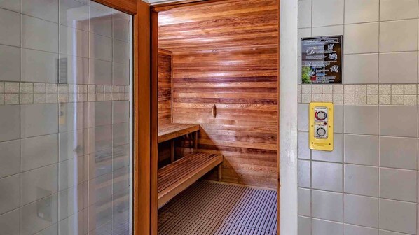 Una sauna con paredes de madera, un banco, suelo de baldosas y un panel de control en la pared.