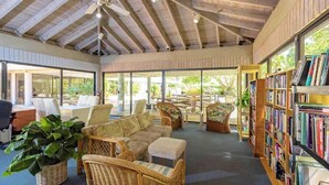 A cozy reading area with wicker furniture, a bookshelf, and large windows allowing natural light. - **SHANG-RI-LA** Oceanview Condo/ Pool & Tennis + Last Key White Glove Service... (Key West)