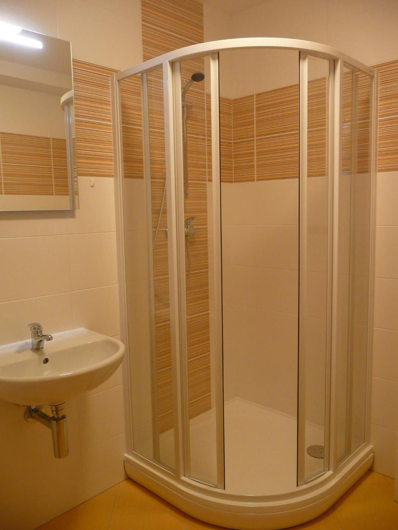 Cabina doccia con porta in vetro, lavandino e specchio a parete.