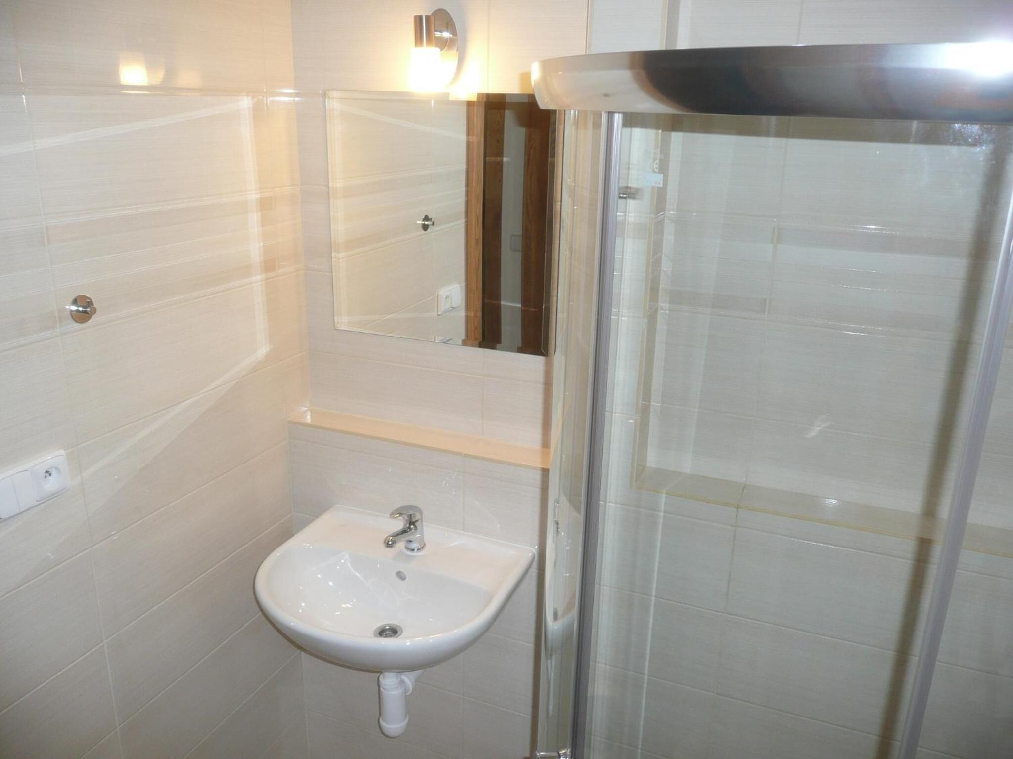 A bathroom with a white sink, a mirror, and a shower enclosure.