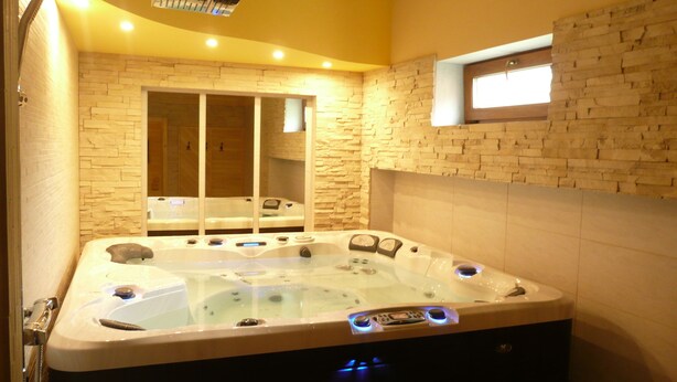 A modern bathroom with a large bathtub, a showerhead, and a stone wall. - Hotel Fojtů (Bruntal)