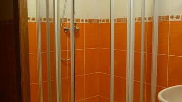 A corner shower with a glass enclosure, orange tiled walls, and a white sink.