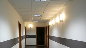 A long, narrow hallway with dark tiled flooring, white walls with a grey stripe, and recessed lighting. - Hotel Fojtů (Bruntal)