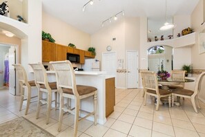 A spacious kitchen with a central island, wooden cabinets, and a dining area with a round table and chairs. - Magical 3BR Pool Home in Oak Island Harbor Close to Parks (Kissimmee)
