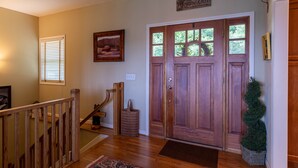 Un escalier en bois mène à une porte ornée d’une pancarte accueillante, à un tableau encadré et à un petit sapin de Noël.
