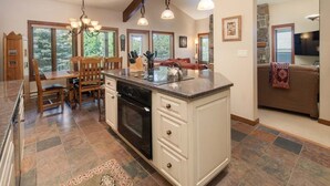 A kitchen with a central island, wooden chairs, a dining table, and a stone fireplace. - JHRL - Slope-side Rendezvous C4 condo, steps from Hot tub, sleeps 9 (Teton Village)