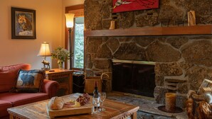 A cozy living room with a stone fireplace, a red sofa, a wooden coffee table with snacks, and a framed wildlife painting on the wall. - JHRL - Slope-side Rendezvous C4 condo, steps from Hot tub, sleeps 9 (Teton Village)