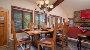 A dining area with a wooden table and chairs, a chandelier, and a stone fireplace. - JHRL - Slope-side Rendezvous C4 condo, steps from Hot tub, sleeps 9 (Teton Village)