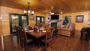 Ein Holzblockhaus-Interieur mit Esstisch, Stühlen, Kamin, Fernseher und Weihnachtsbaum.