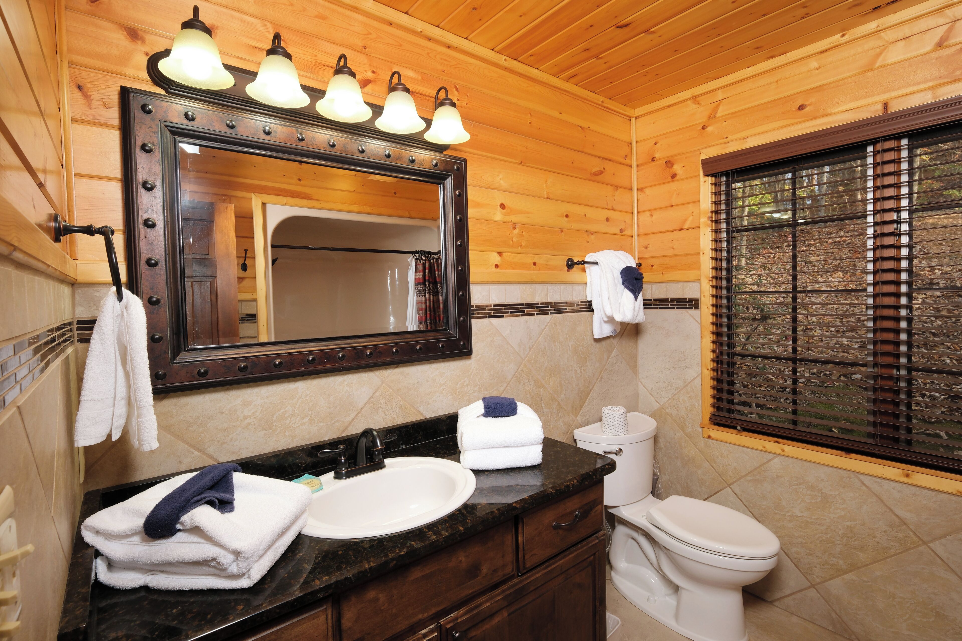 A wooden cabin bathroom with a vanity, sink, mirror, and toilet.