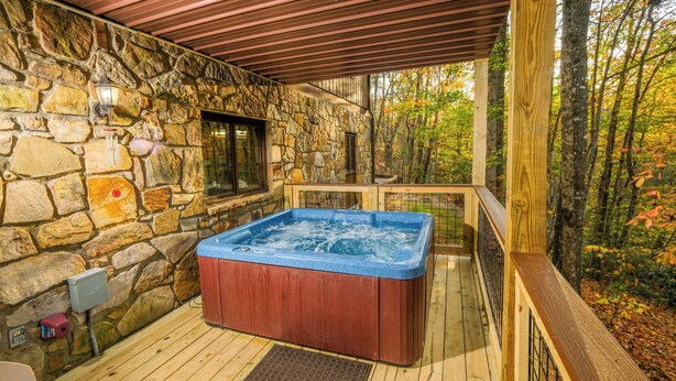 Ein Whirlpoolbereich mit Steinwänden und Holzterrasse, eine Mauer mit Fenster und Blick auf Herbstbäume.
