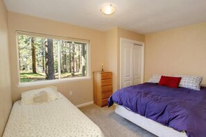 A bedroom with two beds, a dresser, a window with a forest view, and a door.