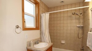 A bathroom with a bathtub, a shower, a sink, and a window.