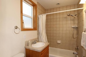A bathroom with a bathtub, a shower, a sink, and a window.