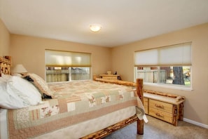 A bedroom with a bed, bedside tables, a window with blinds, and a ceiling light.