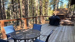 A deck with a round table and chairs, surrounded by a wooden railing, overlooking a forested area.