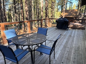 A deck with a round table and chairs, surrounded by a wooden railing, overlooking a forested area.