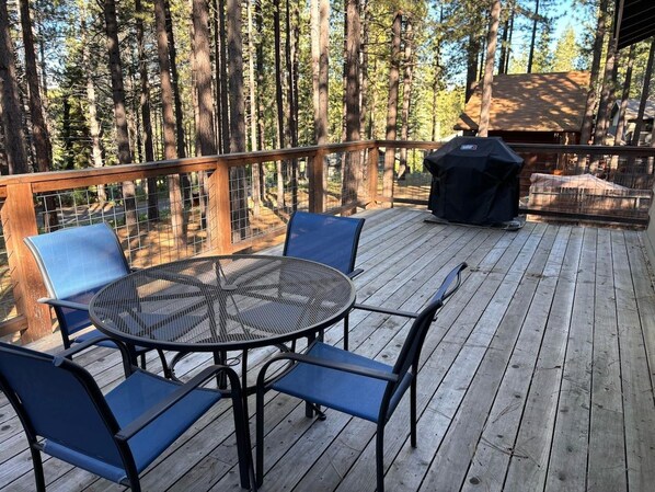A deck with a round table and chairs, surrounded by a wooden railing, overlooking a forested area.