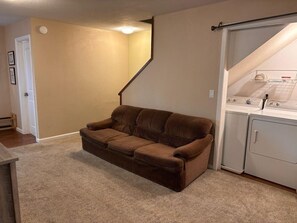 A living room with a brown sofa, a staircase, and a laundry area with a washing machine.